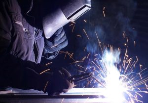 Welder using protective helmet and torch during arc welding with bright sparks flying