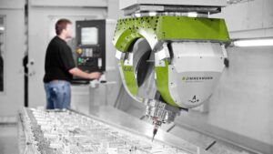 Operator controlling a Zimmermann 5-axis CNC machine performing precision machining on a complex workpiece.